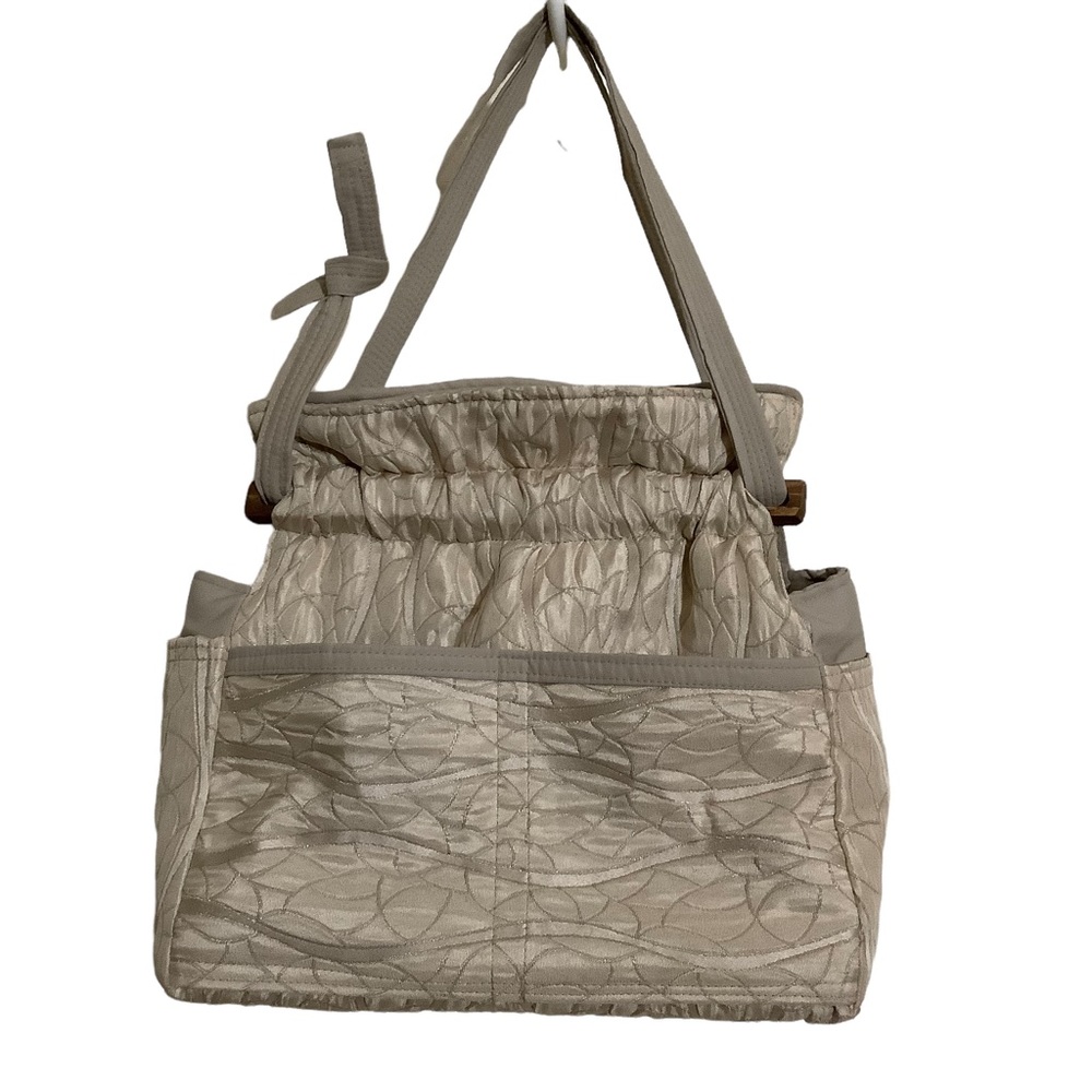 FABRIC SHOULDER BAG WITH OUTSIDE SURROUNDING POCKETS IN A CREAM AND TAUPE COLOR.